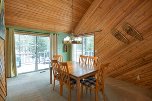 Un espace repas avec une table et des chaises en bois, un lustre et une vue sur l’extérieur.