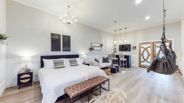 A modern bedroom with a large bed, a hanging chair, a desk with two chairs, and a television.