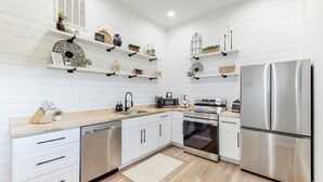 Una cocina moderna con armarios blancos, electrodomésticos de acero inoxidable y objetos decorativos en las repisas.
