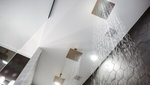 Un baño moderno con piso de baldosas geométricas, techo blanco y múltiples cabezales de ducha.