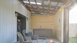 Un espacio exterior techado con sillas de mimbre, un hogar y un jacuzzi.