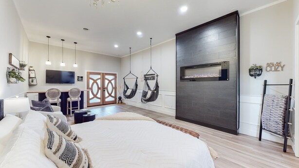 Un dormitorio moderno con una cama grande, un televisor, una chimenea y dos hamacas colgantes.