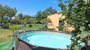 Une piscine avec un escalier, entourée de verdure et bordée d’un bâtiment.