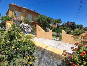 A residential building with a gated entrance, a staircase, and a garden with various flowers.