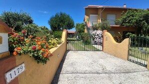 Un immeuble résidentiel doté d’une entrée sécurisée par un portail, d’un escalier menant à l’entrée et d’une variété de fleurs aux couleurs vives le long du mur.