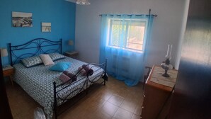 Une chambre à coucher avec un lit, une fenêtre avec des rideaux, une table de chevet, une lampe et un mur décoré de tableaux.