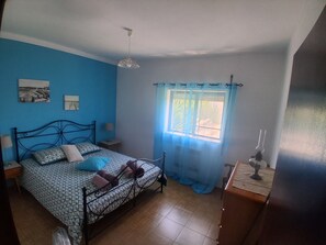 Un dormitorio con cama, una ventana con cortinas, una mesita de noche, una lámpara y una pared decorada con cuadros.