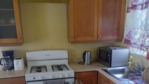 A compact kitchen with a white stove, a microwave, a coffee maker, and wooden cabinets. - Cheerful 2-Bedroom Home in Falmouth Garden (Falmouth)