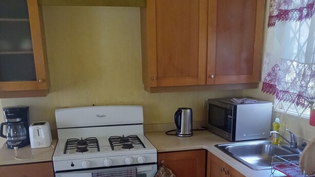 Une cuisine de taille réduite, avec un fourneau blanc, un four à micro-ondes, une machine à café et des armoires en bois.