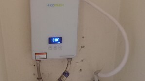 A water heater with a digital display reading 88°F, connected to a white pipe and a red valve. - Cheerful 2-Bedroom Home in Falmouth Garden (Falmouth)