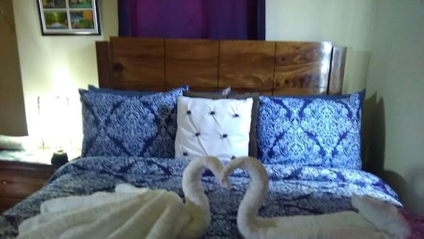 A bed with a patterned bedspread, two pillows, and two towels arranged in a swan shape. - Cheerful 2-Bedroom Home in Falmouth Garden (Falmouth)