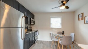 A compact kitchen with dark cabinets, a stainless steel refrigerator, a microwave, and a dining area with a table and chairs. - Melrose Studio - Pool & Free Parking Near Downtown (Nashville)