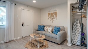 A living room with a grey sofa, a wooden coffee table, and a patterned wall hanging. - Melrose Studio - Pool & Free Parking Near Downtown (Nashville)