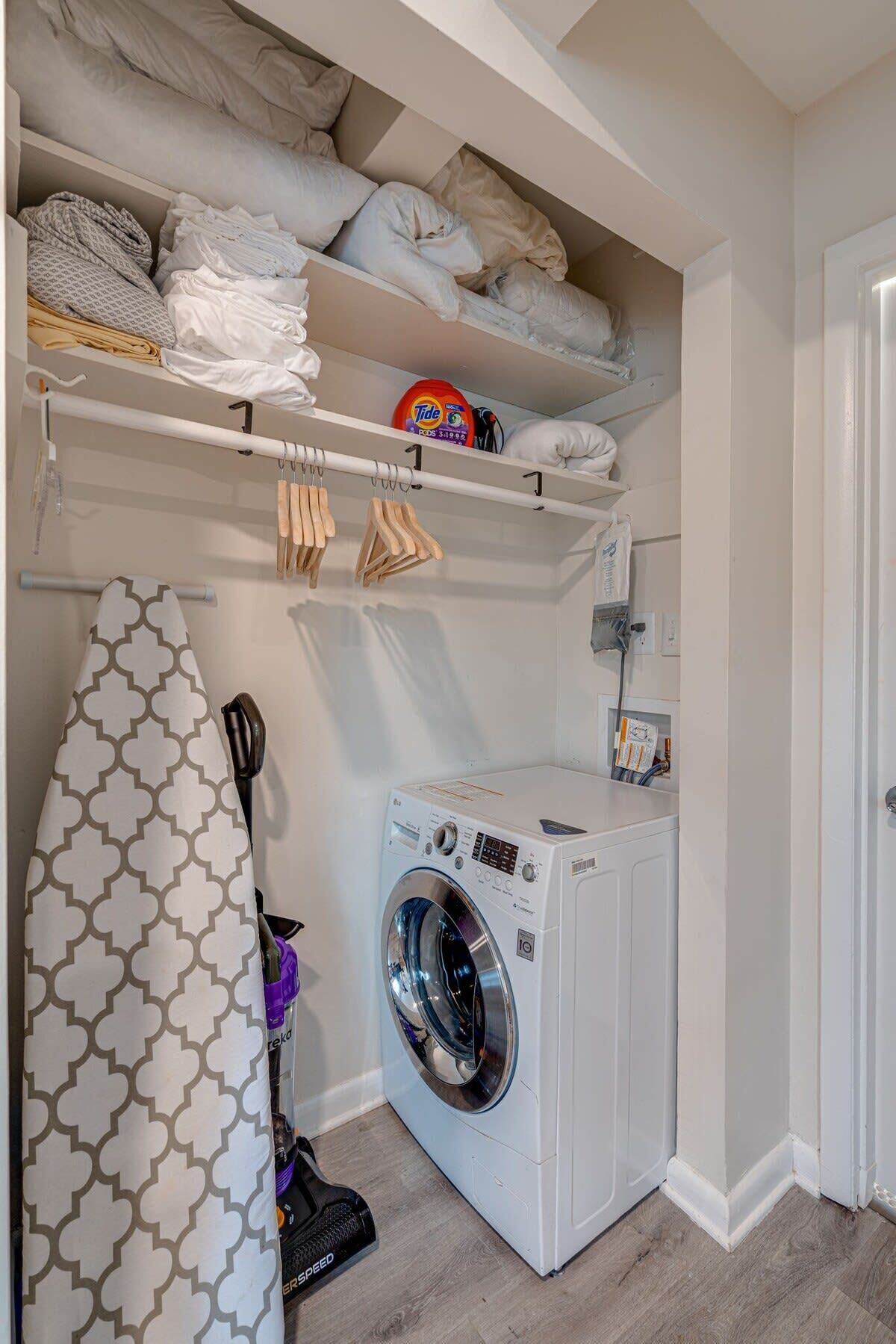 A compact laundry room with a front-loading washing machine, a drying rack, and neatly folded towels on shelves.