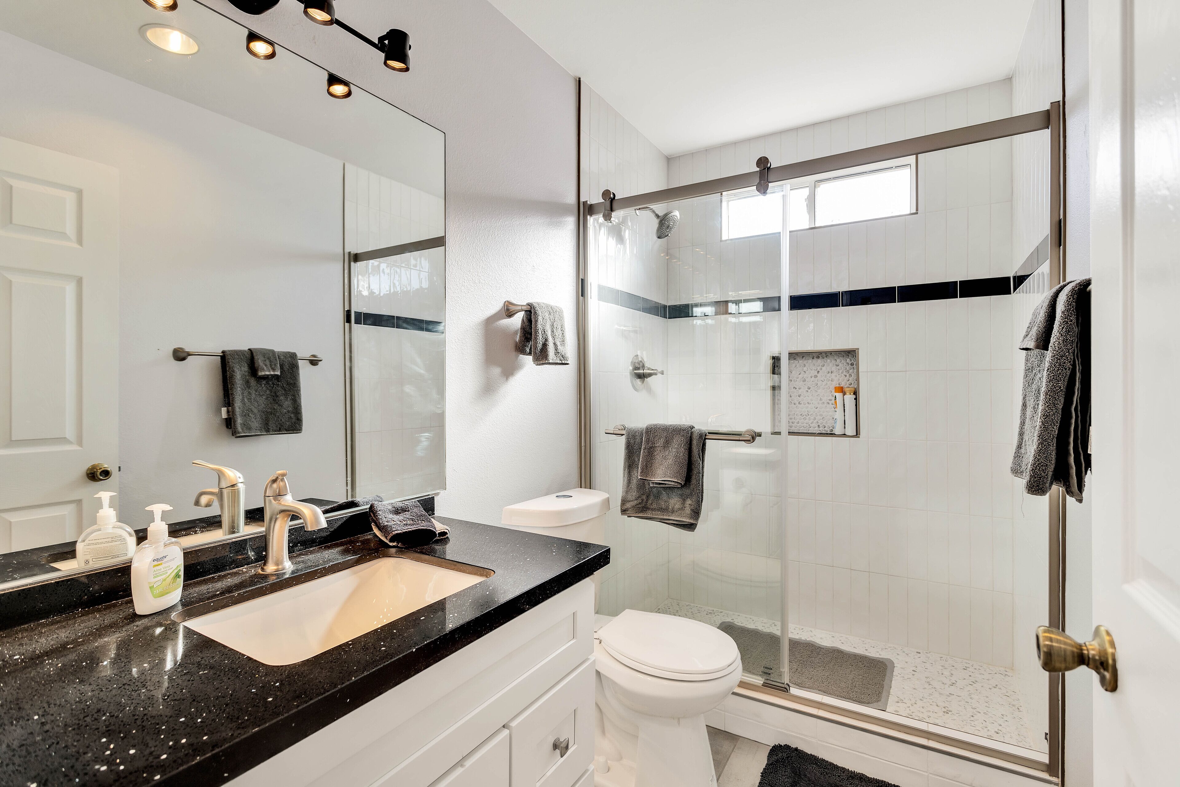 Casa de banho moderna com bancada preta, lavatório branco e zona de duche envidraçada.