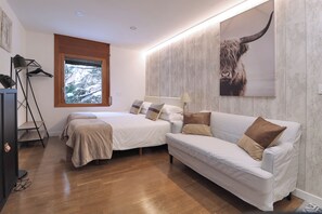 Une chambre avec deux lits, un canapé, une fenêtre donnant sur un beau paysage, une lampe et une œuvre d’art accrochée au mur.