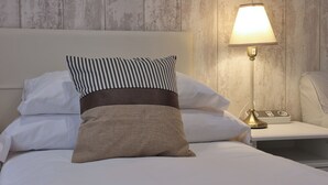 Una cama bien hecha con almohadas a rayas y lisas, una lámpara de noche y una regleta de enchufes en una pared de madera.