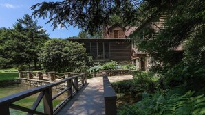 A wooden bridge leading to a rustic cabin surrounded by lush greenery. - Fin & Feather at Seven Springs (Champion)