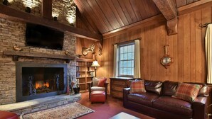 A cozy living room with a stone fireplace, leather sofa, and wooden walls. - Fin & Feather at Seven Springs (Champion)