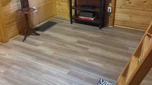 Un interior de madera con un televisor sobre un mueble bajo, una lámpara en una mesita auxiliar y una alfombra estampada.