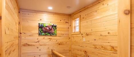 A wooden interior with a wooden staircase, a small window, and a wall-mounted picture.