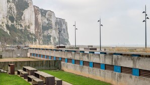 Une promenade en bord de mer, agrémentée de bancs et d’une barrière en béton aux touches de bleu.
