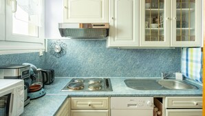 Une cuisine avec des meubles blancs, un plan de travail bleu et divers appareils, notamment un grille-pain, une bouilloire et une cuisinière.