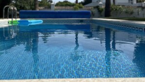 Une piscine à l’eau d’un bleu cristallin, entourée de palmiers et avec un bâtiment blanc en arrière-plan.
