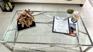 Un salon avec une table basse en verre, un canapé beige agrémenté de coussins à motifs et une petite plante en pot.