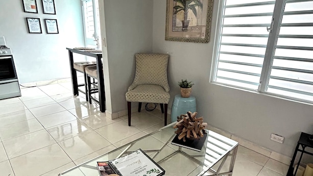 Un salon moderne avec une table basse en verre, un fauteuil à motifs, une plante en pot et un tableau encadré accroché au mur.