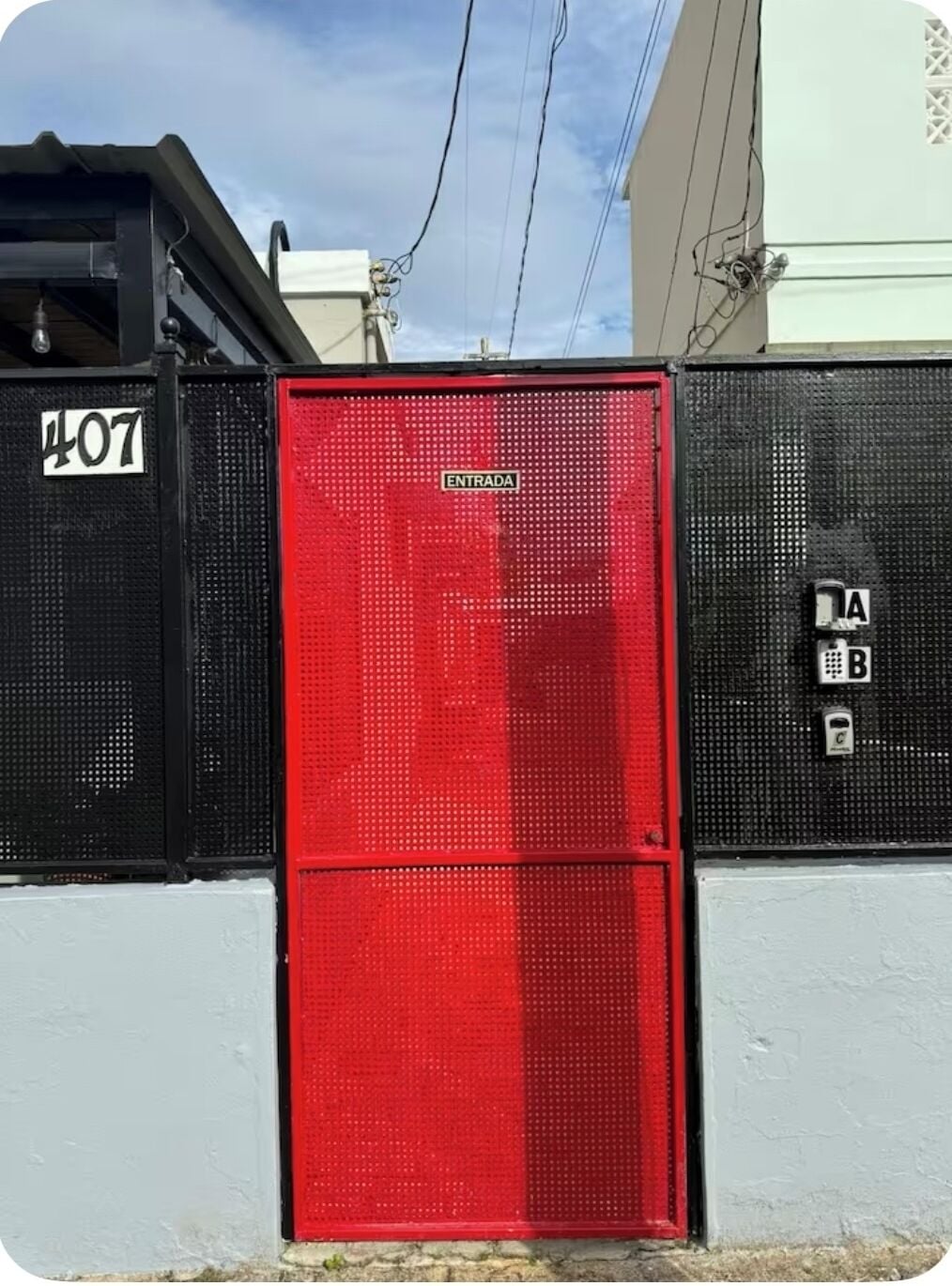 Une boîte métallique rouge contenant des équipements techniques, avec une pancarte indiquant « ENTRADA » et un clavier doté de boutons étiquetés « A » et « B ».