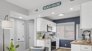 A modern kitchen with white cabinets, a stove, and a microwave. There is a sign above the cabinets that reads "BEACH HOUSE". - A Little Shore Thing 1 Bedroom Condo by RedAwning (Carolina Beach)