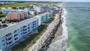 A coastal hotel with multiple floors, a beachside location, and a pier in the background. - A Little Shore Thing 1 Bedroom Condo by RedAwning (Carolina Beach)