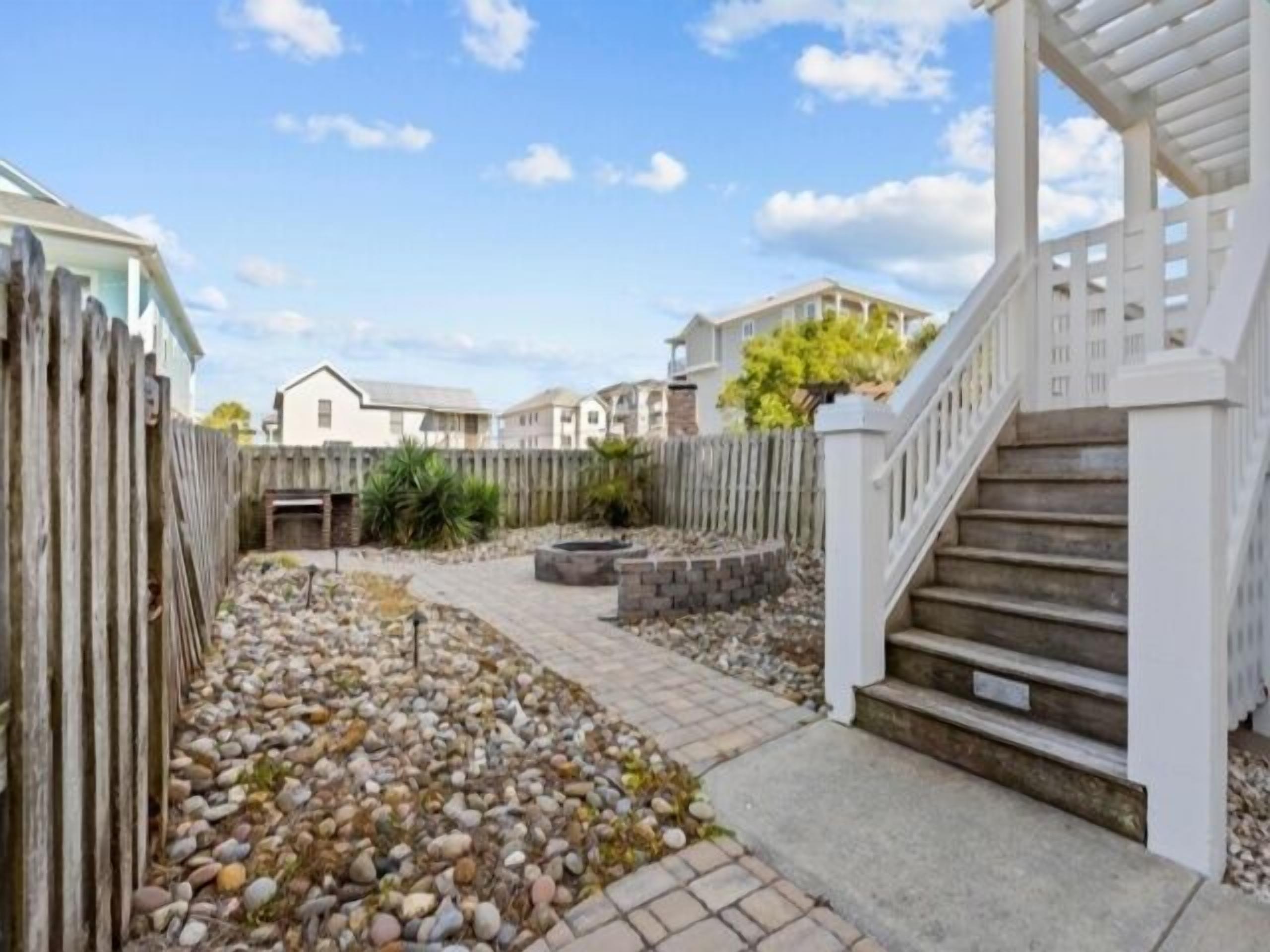 A residential area with a paved pathway, a wooden fence, and a staircase leading to a covered porch.