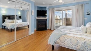 A bedroom with a bed, a TV, a fireplace, and a balcony. - Almost Heaven 4 Bedroom Home by RedAwning (Carolina Beach)