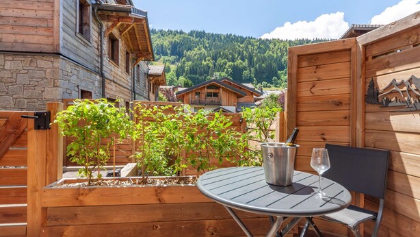 Una terraza de madera con una mesa y sillas, rodeada por una valla de madera y un jardín.