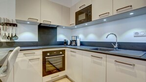 Una cocina moderna con armarios blancos, horno empotrado, cafetera y pileta de acero inoxidable.