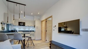 Una cocina moderna con iluminación colgante, un comedor con sofá y sillas, y un televisor de pantalla plana montado en la pared.