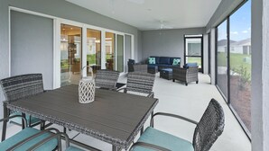 Een overdekt terras met een eettafel en stoelen, een bank en een plafondventilator.
