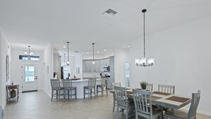 Een ruime keuken met een centraal eiland, moderne hanglampen en een eethoek met een grote tafel en stoelen.
