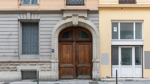 Un bâtiment doté d’une grande porte à double battant en bois, d’une fenêtre avec des volets et d’une petite fenêtre sur laquelle est apposée une enseigne.