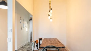 Un couloir étroit avec une table et des chaises en bois, un tapis à motifs et des lampes suspendues.