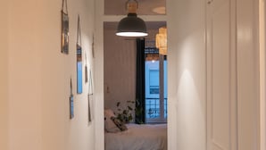 Un couloir étroit mène à une chambre à coucher qui contient un lit, un luminaire suspendu et une fenêtre donnant sur un balcon.
