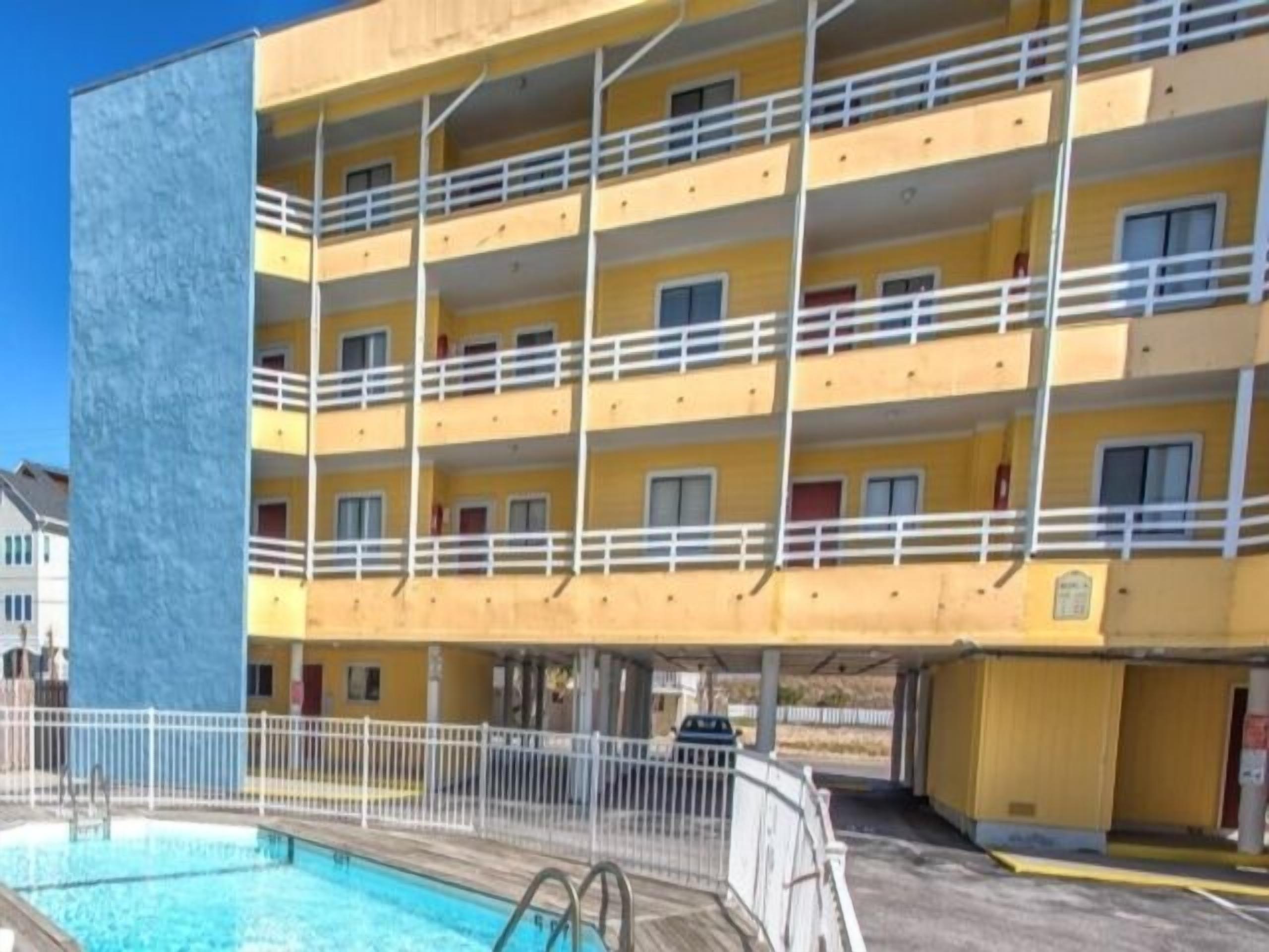 Un hotel de varios pisos con balcones, piscina y zona de estacionamiento.
