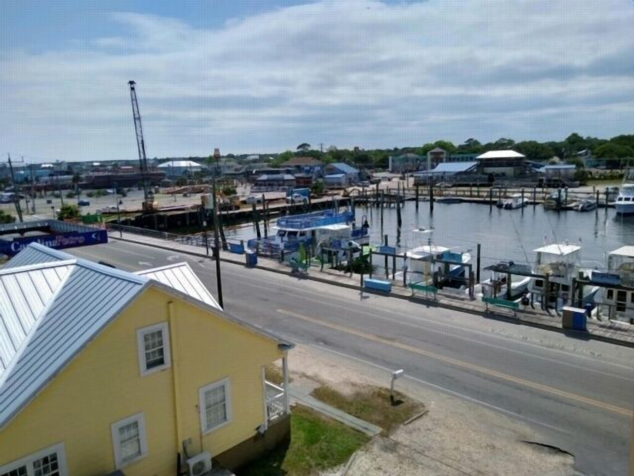 A yellow building with a metal roof, a dock with boats, and a marina in the background.