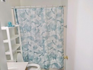 Un baño con cortina de ducha estampada con hojas, un inodoro blanco y una estantería blanca.