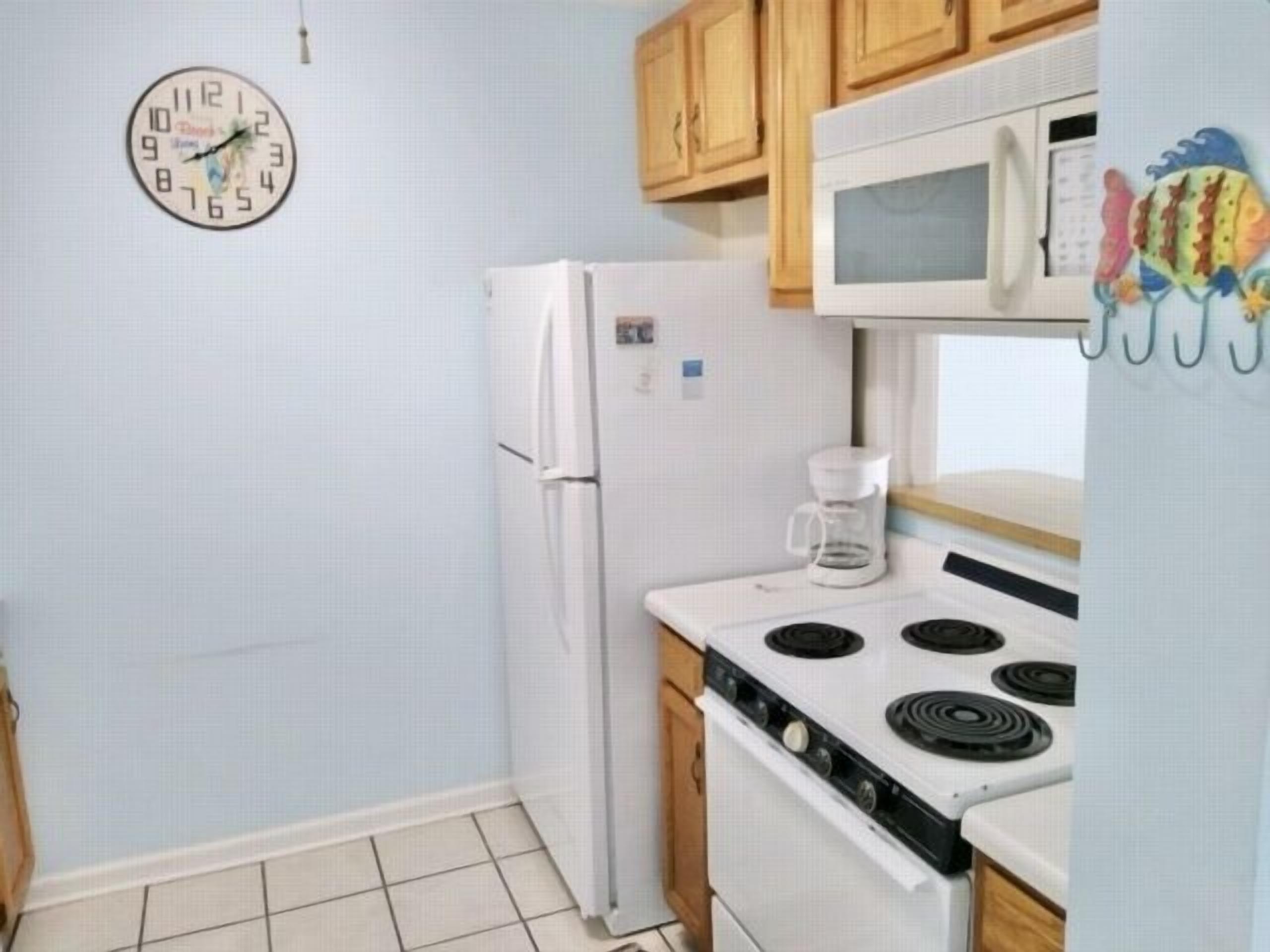 A small kitchen with a refrigerator, microwave, stove, and a clock on the wall.