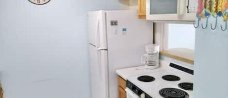A small kitchen with a refrigerator, microwave, stove, and a clock on the wall.