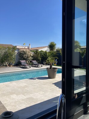 A poolside view with a clear blue sky, a tiled deck, lounge chairs, and a potted palm tree. - Villa Les Sables, Ile de Ré, a few minutes from the ocean (Sainte-Marie-de-Ré)