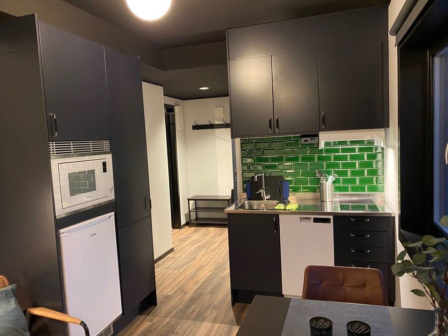 A modern kitchen with dark cabinets, a microwave, a sink, and a green tiled backsplash.